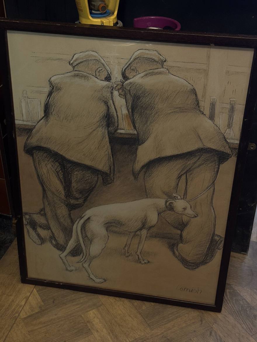 A framed Norman Cornish charcoal print, depicting two cloth-capped drinkers stooped at a bar with a whippet at their feet, propped on a parquet floor inside The Whippet EC2 ahead of being hung.